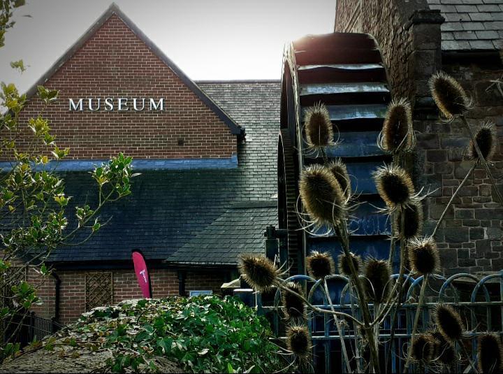 The exterior of the museum building with a watewheel and teasels in the foreground