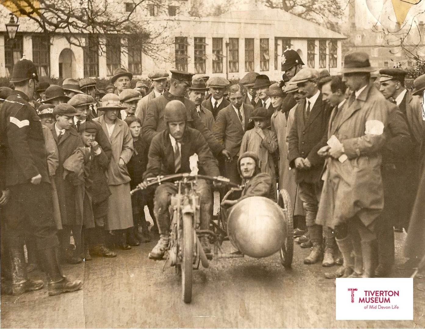 An old fashioned motorbike and sidecar with a crowd of people