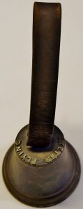 A small bell with a leather strap and the words 'Exeter Flying' visible at the top of the bell. One assumes that the word 'Post' is hidden by the leather handle. 