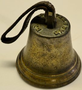 Another small bell with a leather strap used to hold and ring the bell. The words 'Exeter Gazette' are visible at the top of this bell. 