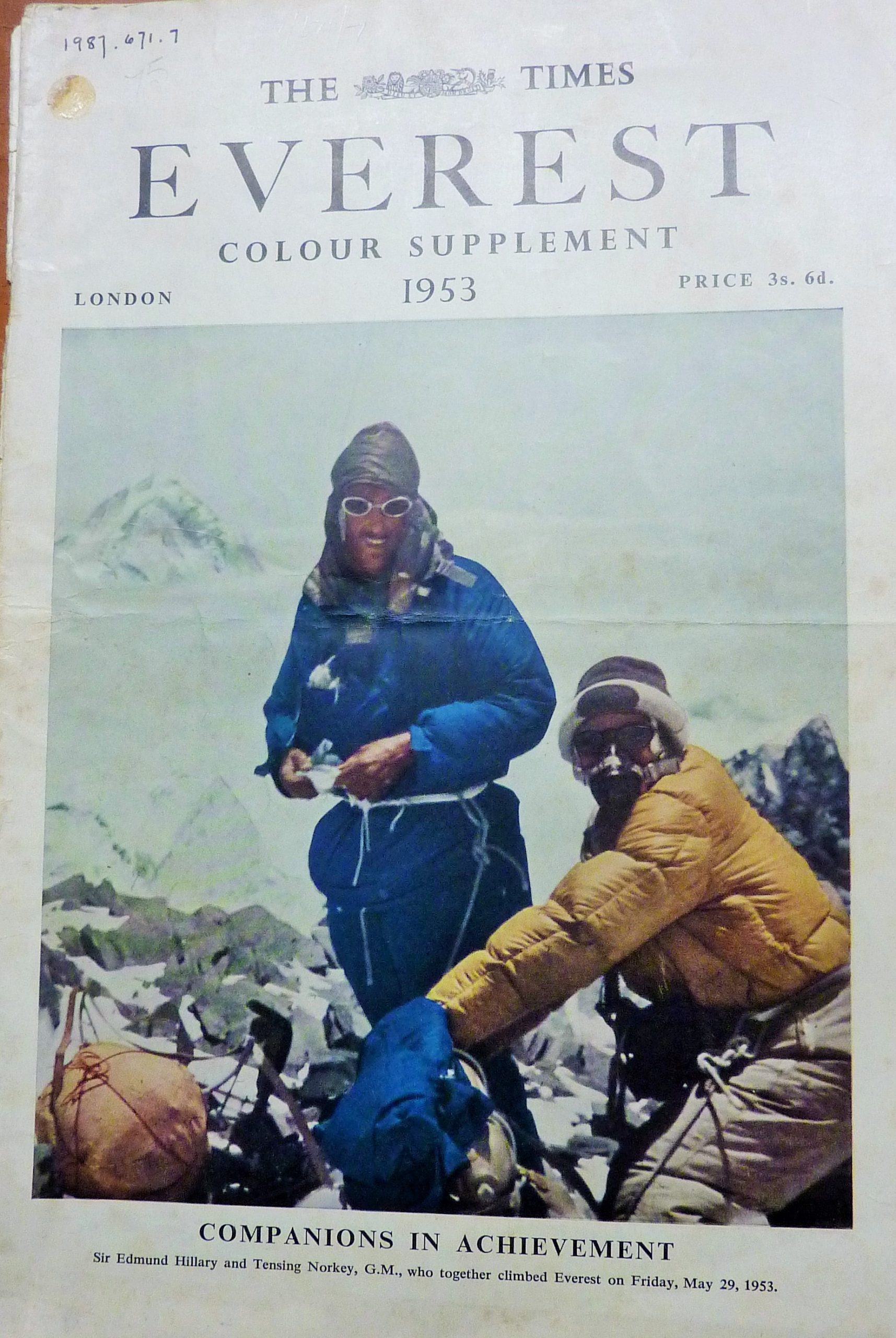 The front cover of 'The Times Everest Colour Supplement 1953'. There is a large colour photo that takes up most of the page, of two men in cold weather gear looking at the camera with snow capped mountains behind them. The cold weather clothing is bright and bulky, one man is in bright blue, the other in yellow, and it looks quite dated compared to similar gear today. One is wearing an oxygen mask and they have ropes attached to their waists. It is captioned 'Companions in Acheivement - Sir Edmund Hillary and Tensing Norkey (sic) who together climbed Everest'. The supplement is priced at 3s. 6d. and their is a museum accession number in the top left.