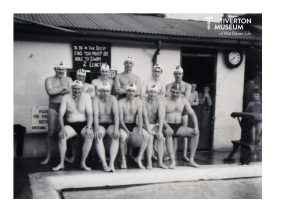 A water polo team sitting next to a swimming pool. They are wearing swimming trunks and tight water polo caps that have stings tied under the chin. There is a sing on the building behind them that read 'To be in the deep end you must be able to swim 2 lengths'. 