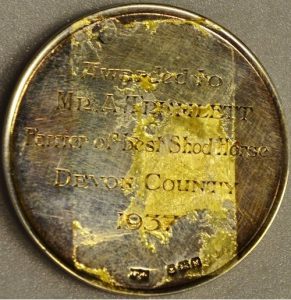 A battered looking medal that bears the inscription 'Awarded to Mr. A. Tremlett Farrier of Best Shod Horse. Devon County 1937